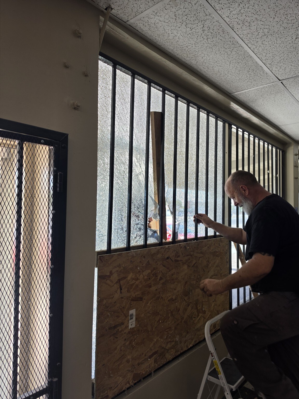 A person positioning a board inside the damaged storefront window at For The Birds and More
