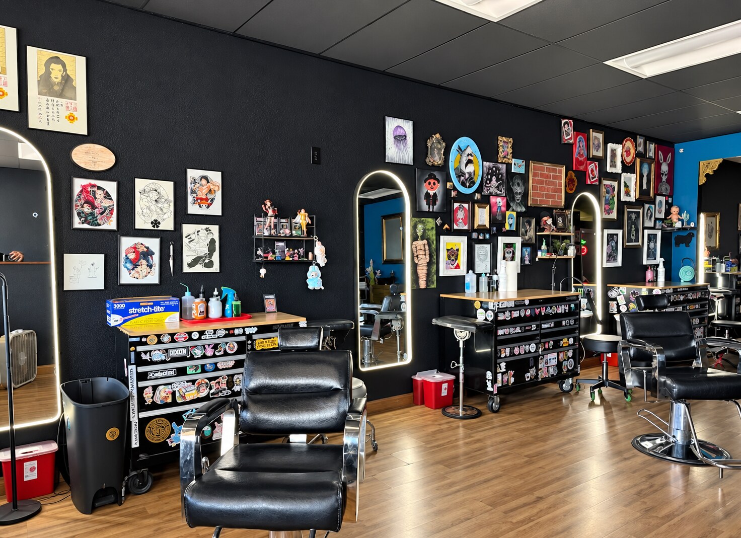 Interior of Voodoo Lily Tattoo with black walls, framed tattoo art, illuminated mirrors and tattoo chairs