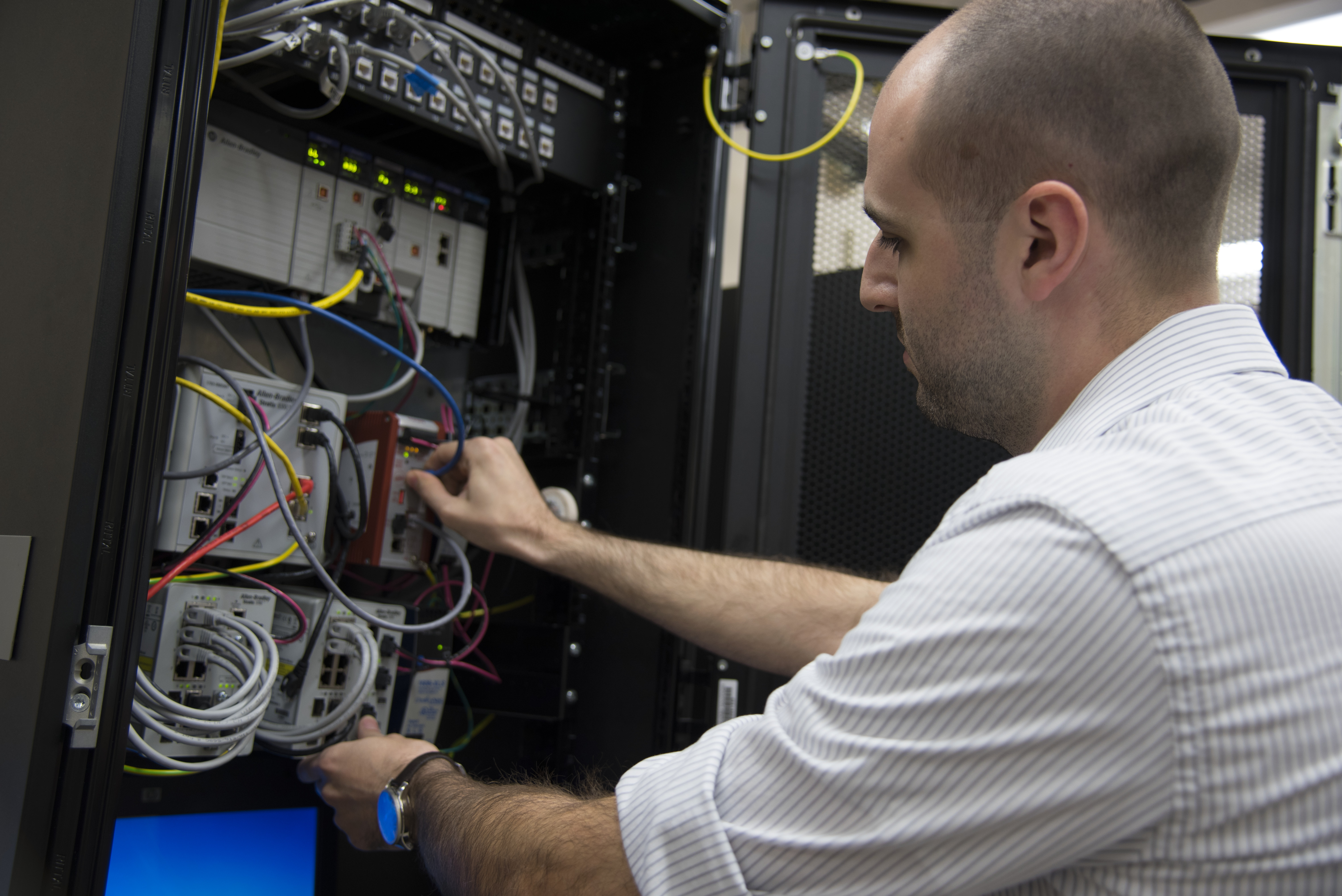 A NIST researcher checks cable connections in industrial control and networking equipment. Archival 2017 context photograph, not a system examined in the 2026 audit.