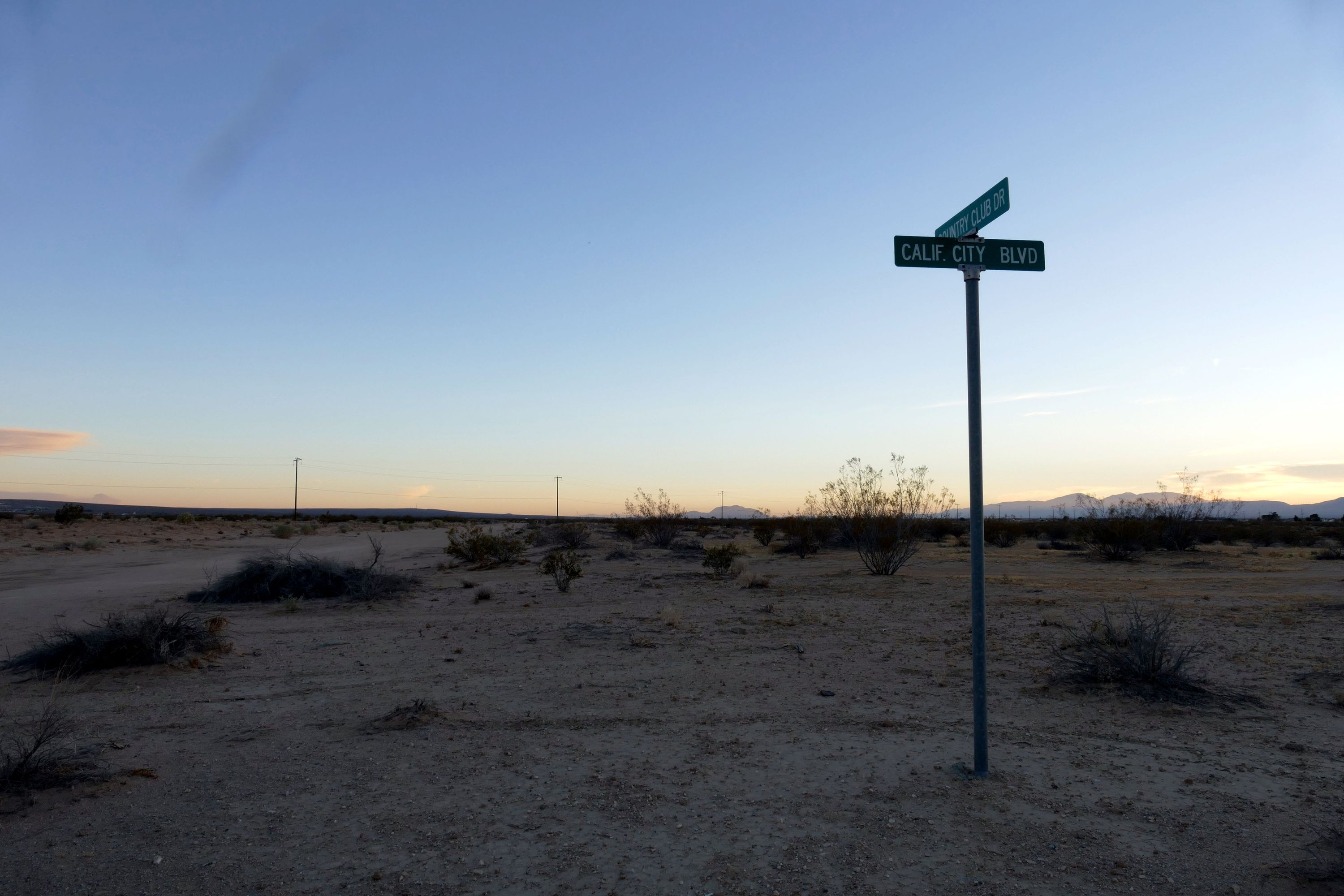 California City Boulevard street sign above an unpaved desert road, with distant mountains.