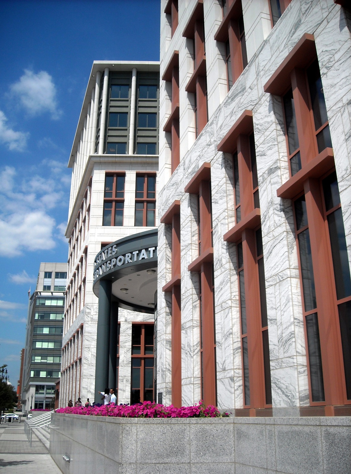 The Department of Transportation headquarters entrance in Washington, D.C., with a curved sign, stone facade and pink flowers in 2008.