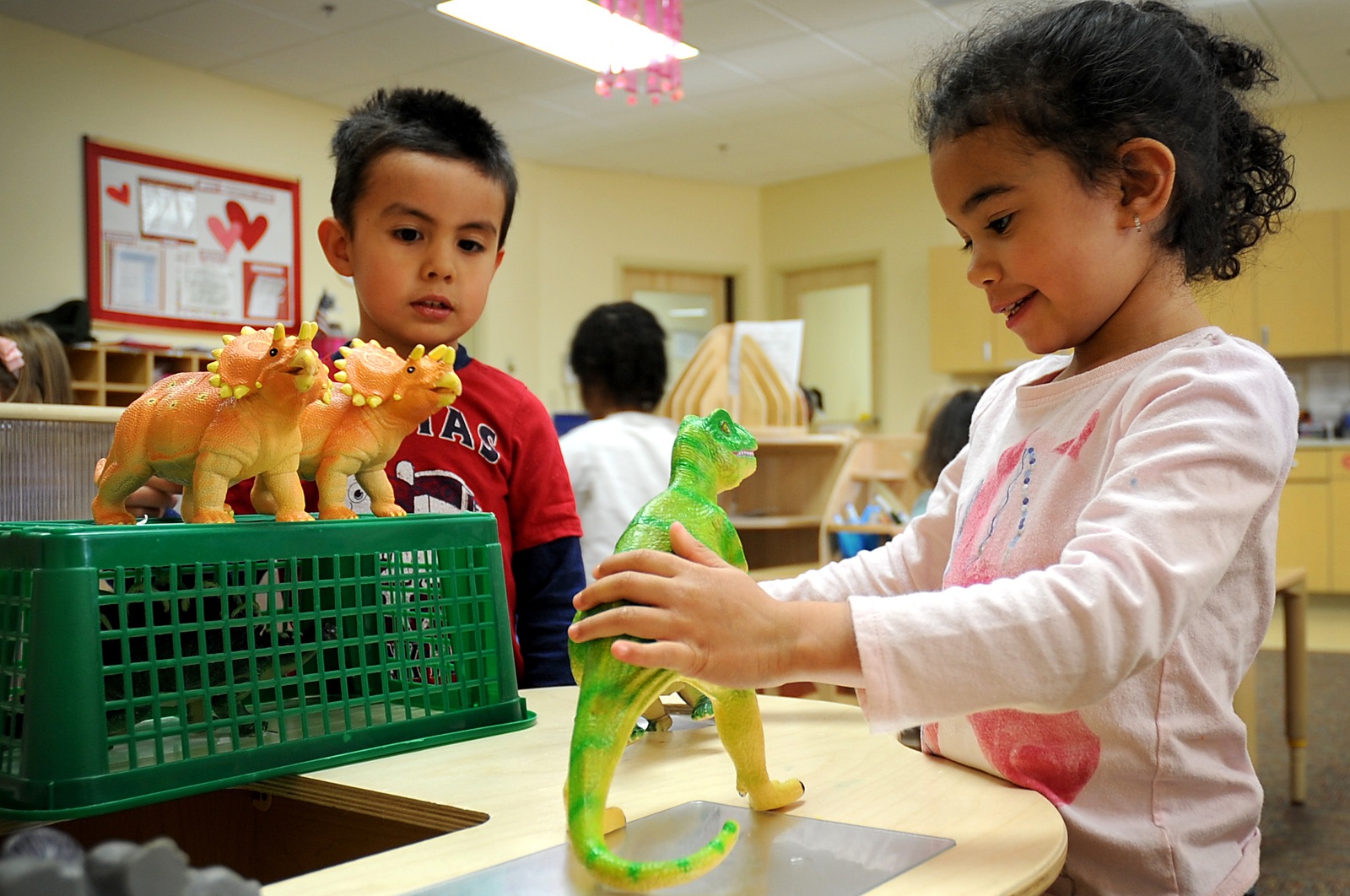 Children playing with colorful dinosaur toys at a table in the Cannon Air Force Base Child Development Center in New Mexico.