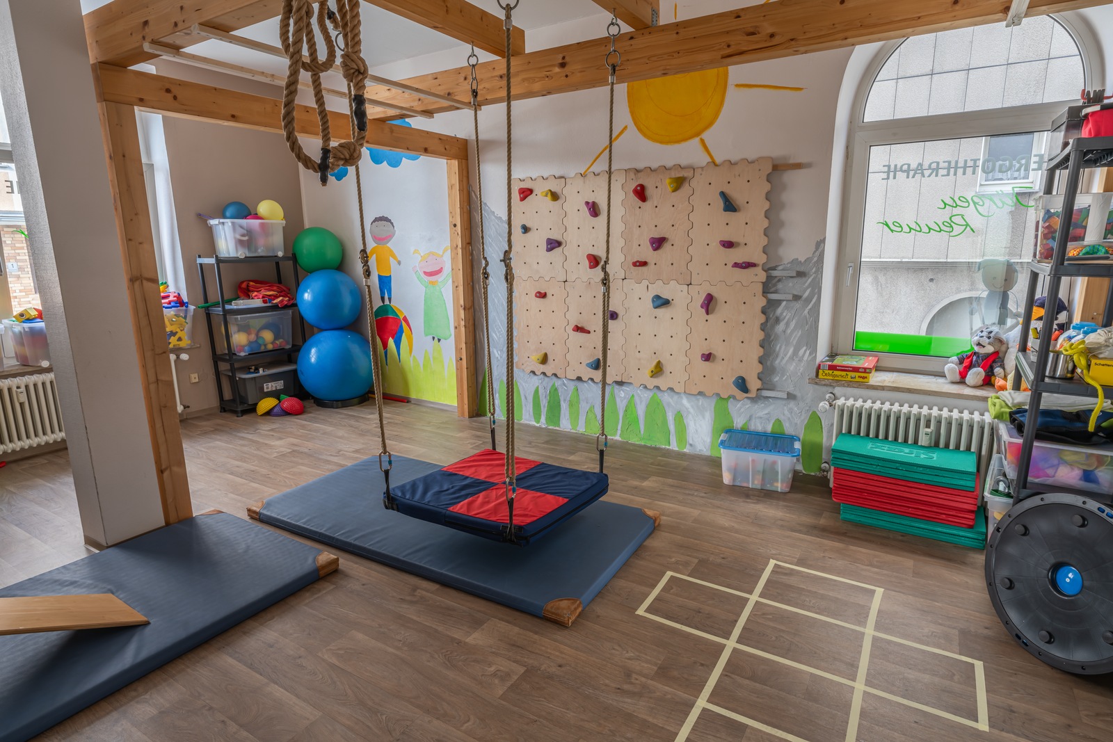 An empty occupational-therapy activity room with padded mats, exercise equipment and a climbing wall.