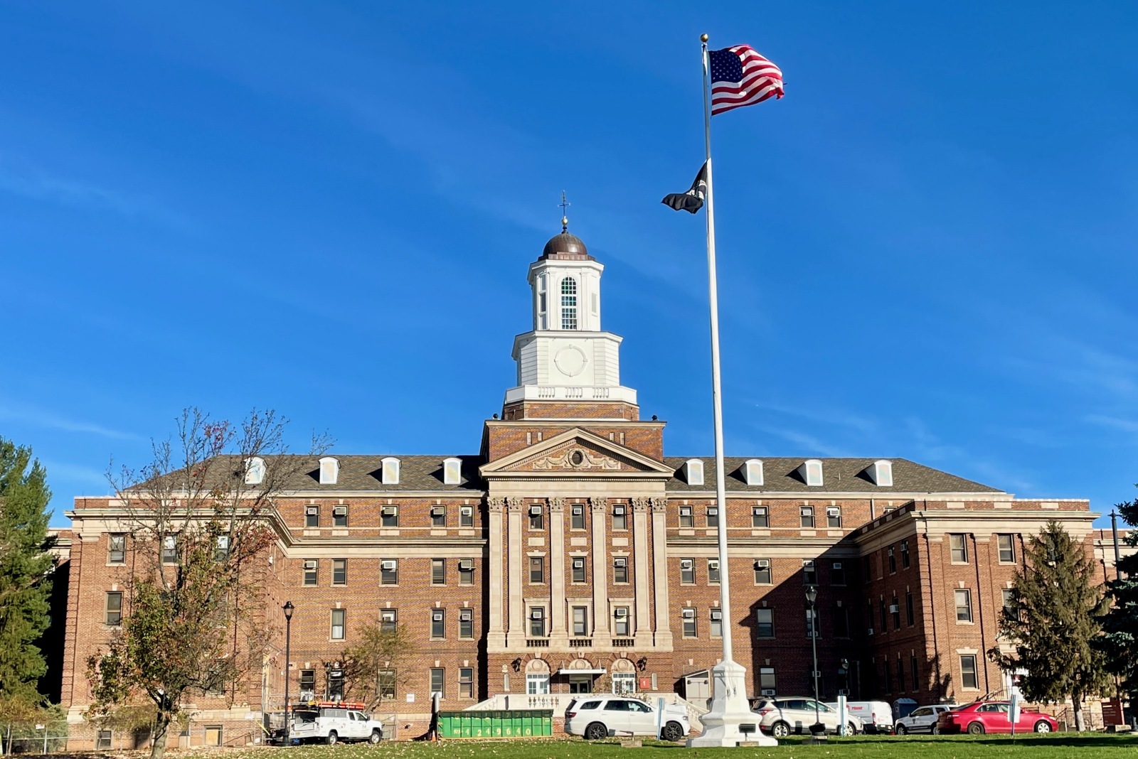 The brick main building at the Lyons VA Medical Center in New Jersey, with a cupola, flagpole and parked vehicles, photographed in 2022.