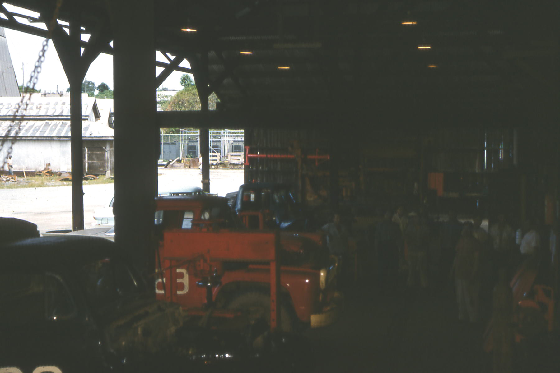 An archival vehicle-maintenance shop with trucks parked inside and beside an open-sided garage.
