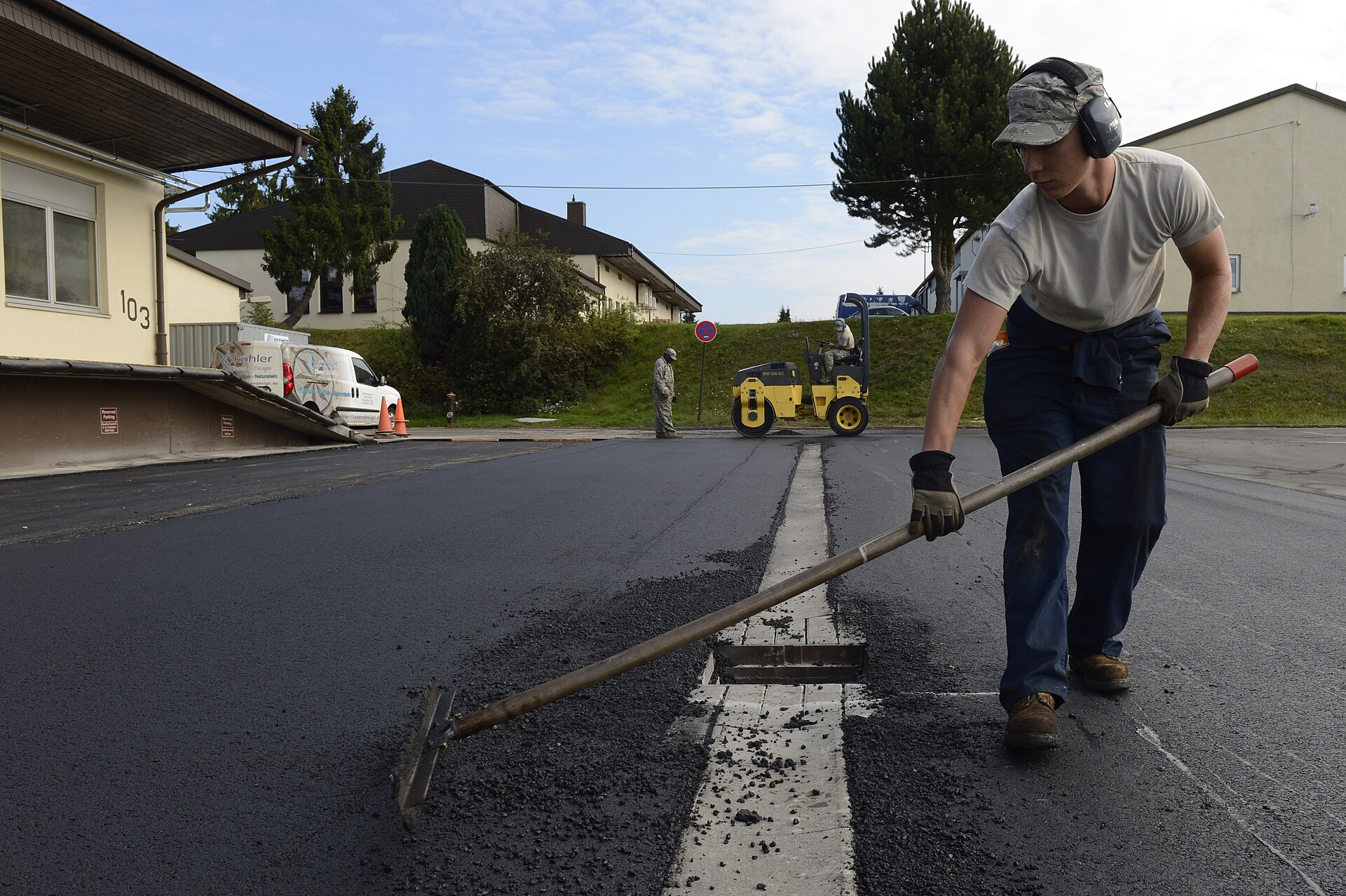 A road worker guides asphalt placement beside paving equipment on a roadway.