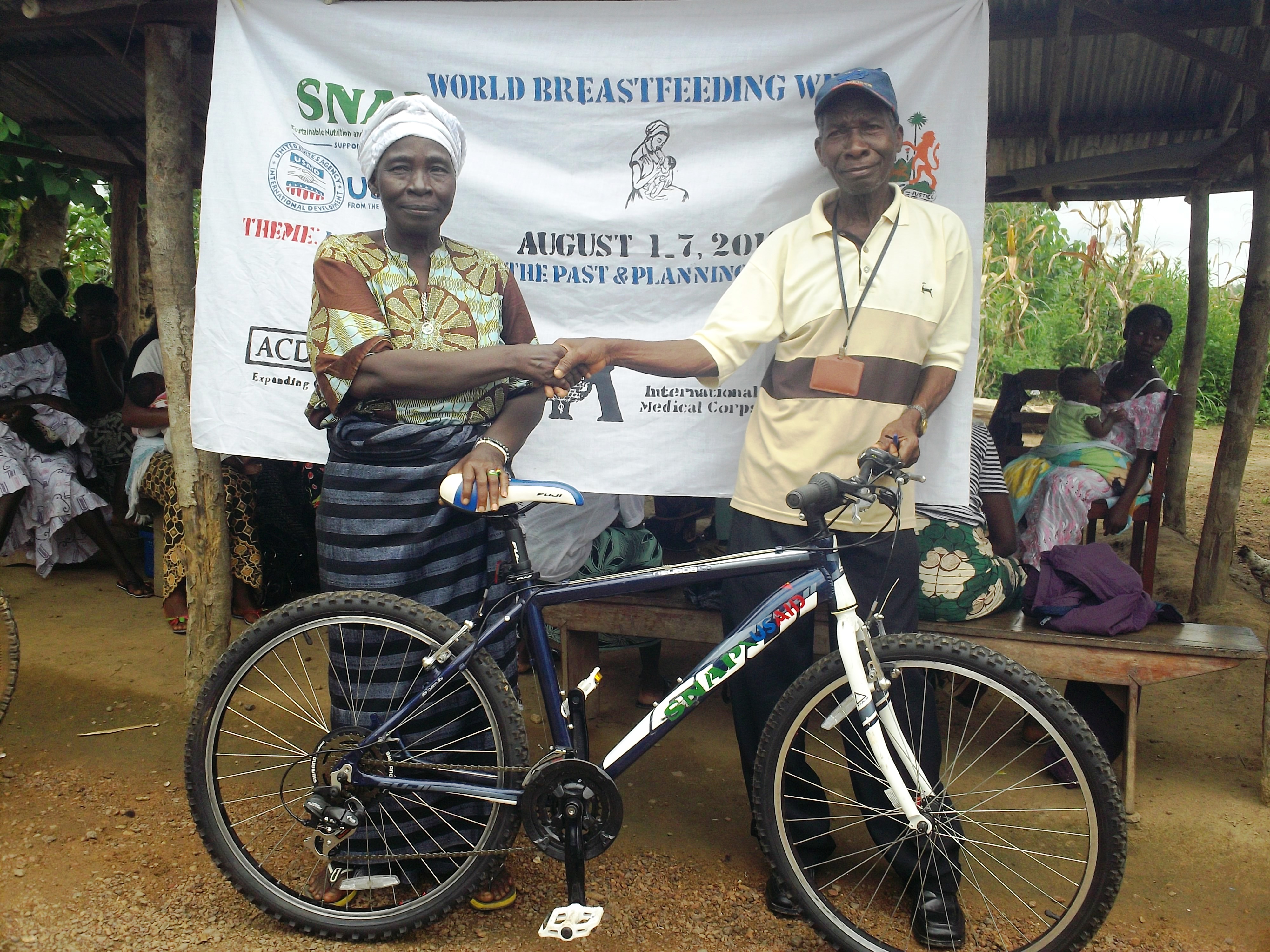 Health promoters with bicycles meet residents on a rural road in Sierra Leone.