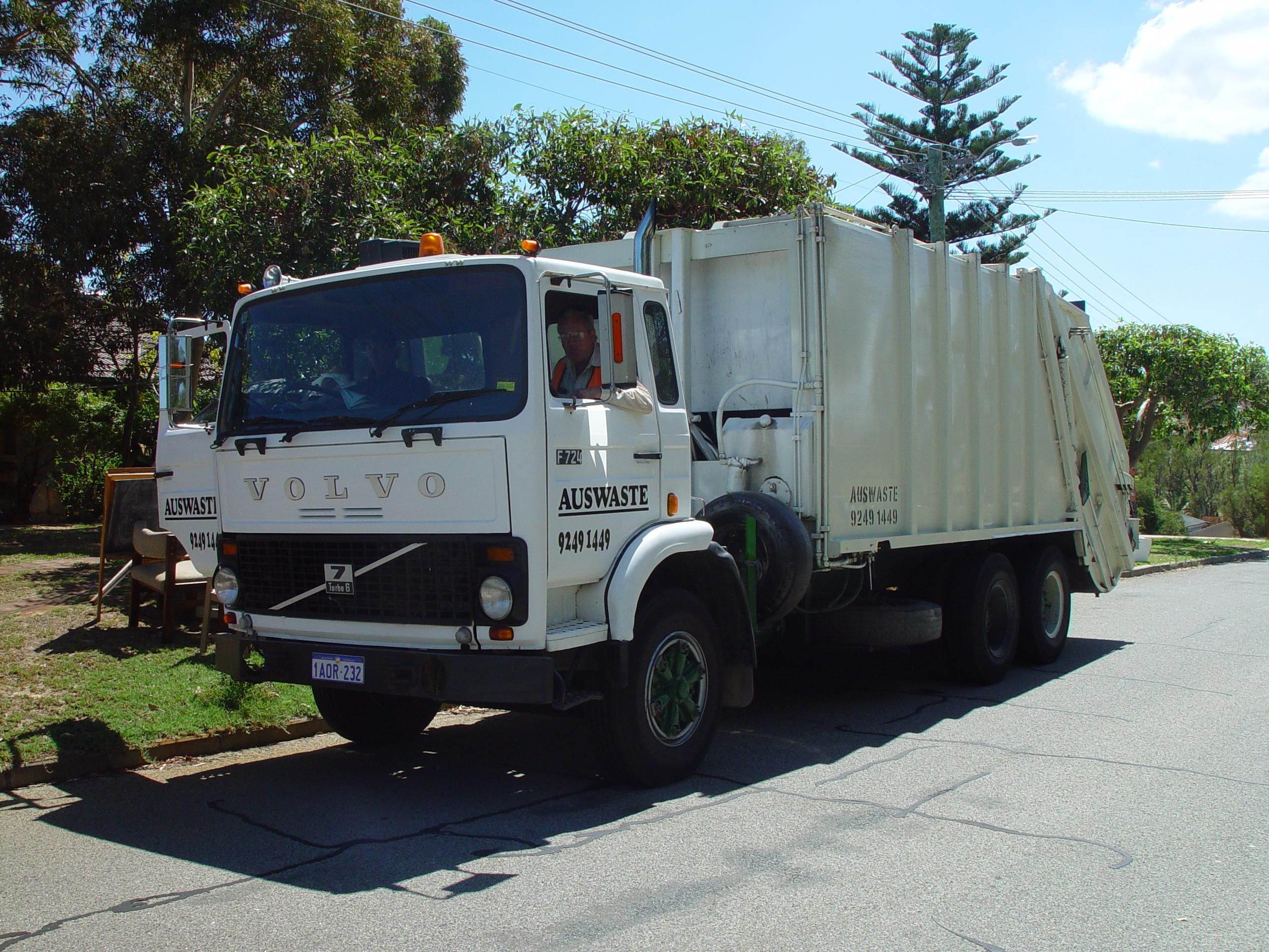 A white garbage collection truck drives on a public road.