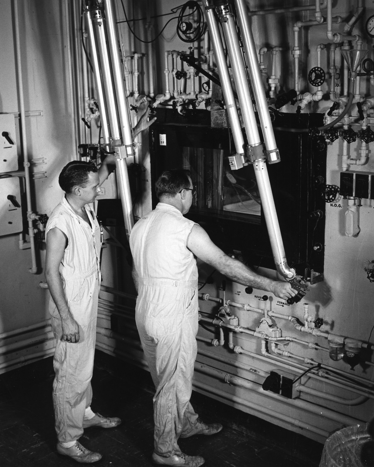 Oak Ridge National Laboratory technicians use remote manipulators behind thick shielding to prepare cobalt-60 teletherapy sources in a hot cell in 1957. Archival isotope-production context; not the present actinium-225 line. Photo: Ed Westcott / U.S. Atomic Energy Commission, public domain.